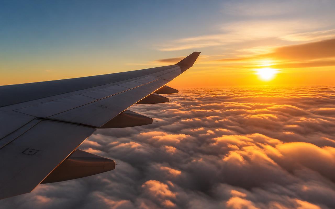 Airplane wing above golden clouds at sunset